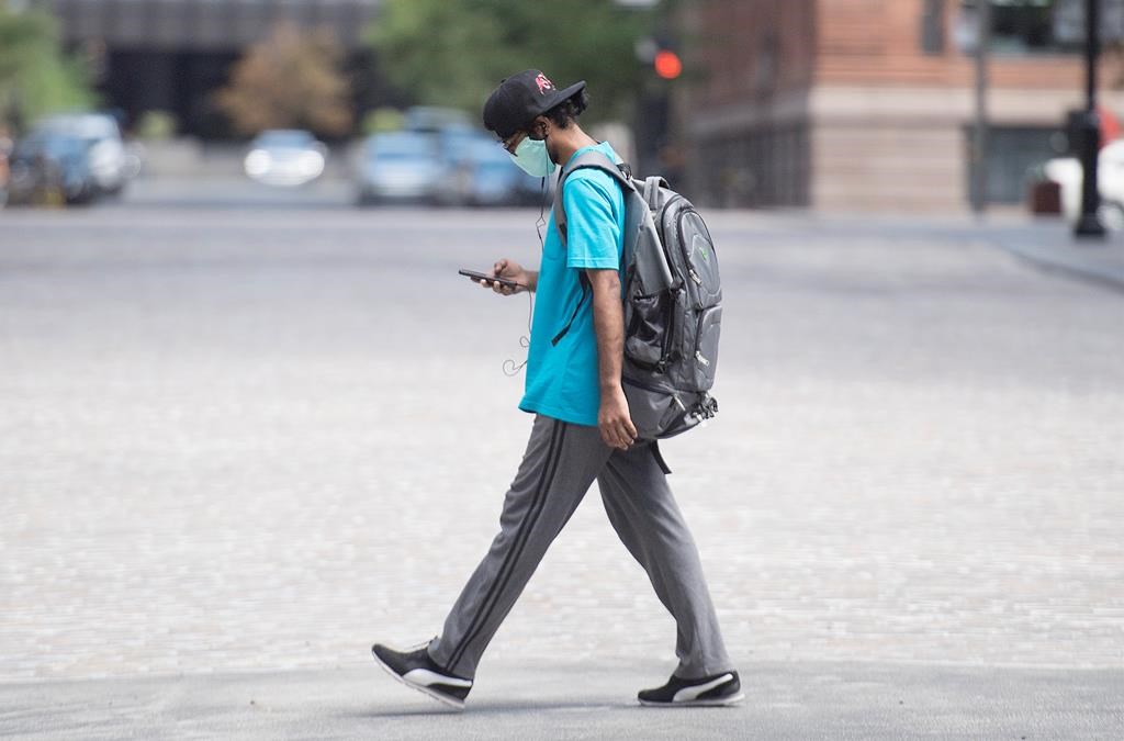 A man wears a face mask as he walks along a street in Montreal, Sunday, July 26, 2020, as the COVID-19 pandemic continues in Canada and around the world.