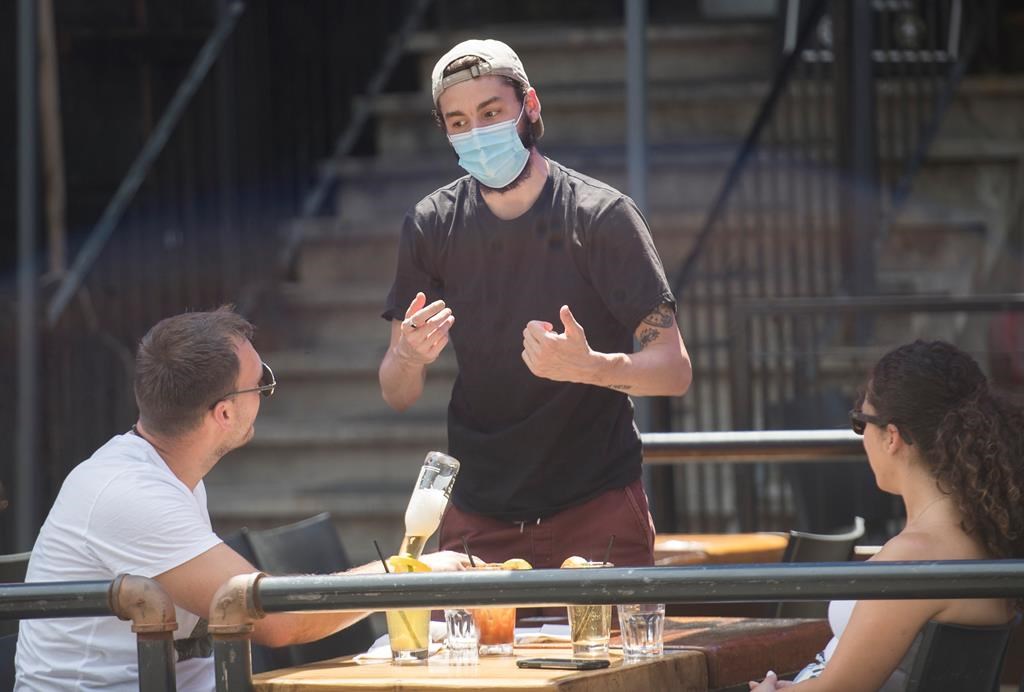 A server wears a face mask as he talks with customers at a bar on a pedestrianised zone of Crescent Street in Montreal, Saturday, July 25, 2020.