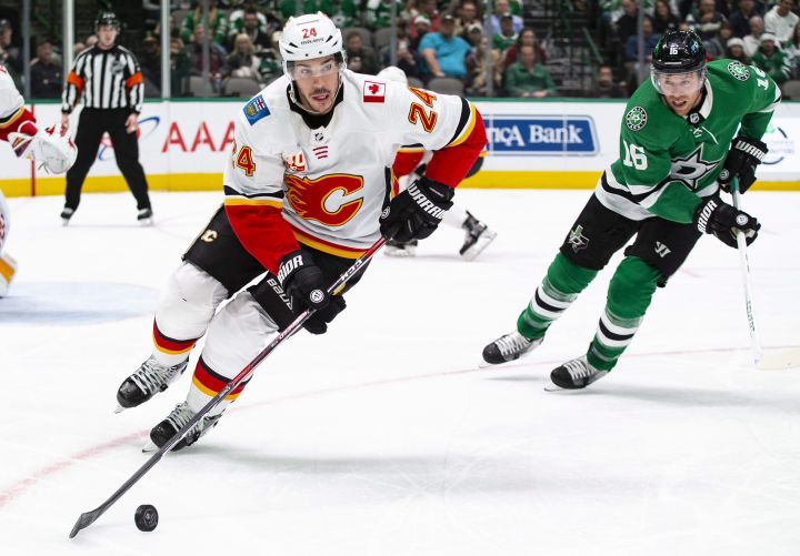Calgary Flames defenseman Travis Hamonic (24) skates with the puck as Dallas Stars center Joe Pavelski (16) pursues during the first period of an NHL hockey game, Sunday, Dec. 22, 2019, in Dallas. 
