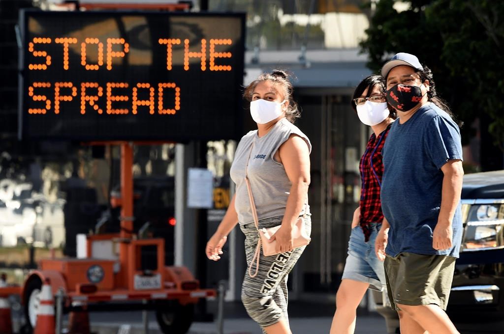 FILE - Pedestrians wear masks as they walk in front of a sign reminding the public to take steps to stop the spread of coronavirus, Thursday, July 23, 2020, in Glendale, Calif.  (AP Photo/Chris Pizzello, File).