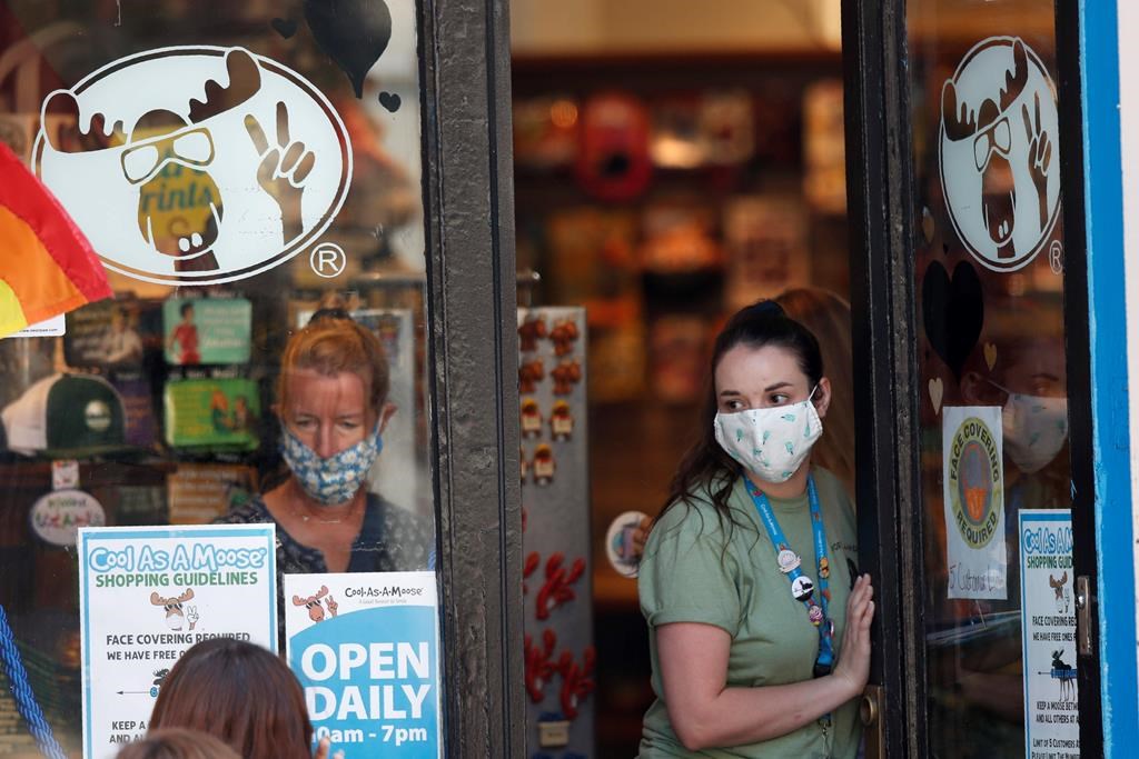 A worker at a gift shop regulated the number of customers allowed in the store due to the coronavirus pandemic, Thursday, July 30, 2020, in Portland, Maine. State officials reported more cases of COVID-19. (AP Photo/Robert F. Bukaty).