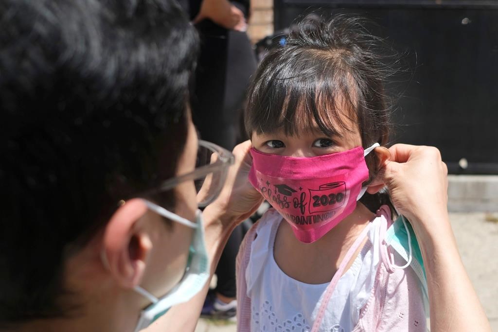 FILE - In this June 10, 2020, file photo, Olivia Chan's father helps her with a new mask she received during a graduation ceremony for her Pre-K class in front of Bradford School in Jersey City, N.J. As the Trump administration pushes full steam ahead to force schools to resume in-person education, public health experts warn that a one-size-fits-all reopening could drive infection and death rates even higher. (AP Photo/Seth Wenig, File).
