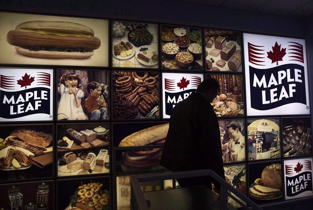 A Maple Leaf Foods employee walks past a Maple Leaf sign at the company's meat facility in Toronto. The company confirmed Wednesday an employee at its Brandon plant has tested positive for COVID-19.