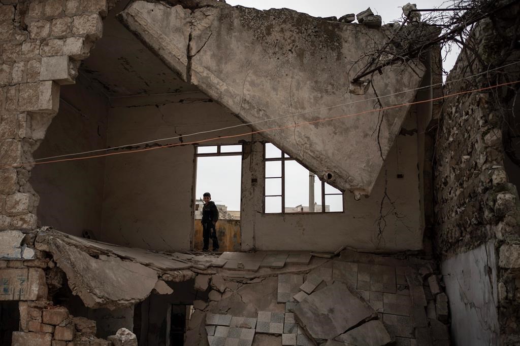 In this Thursday, March 12, 2020 photo, a boy stands inside a house destroyed by an airstrike, in Idlib, Syria.