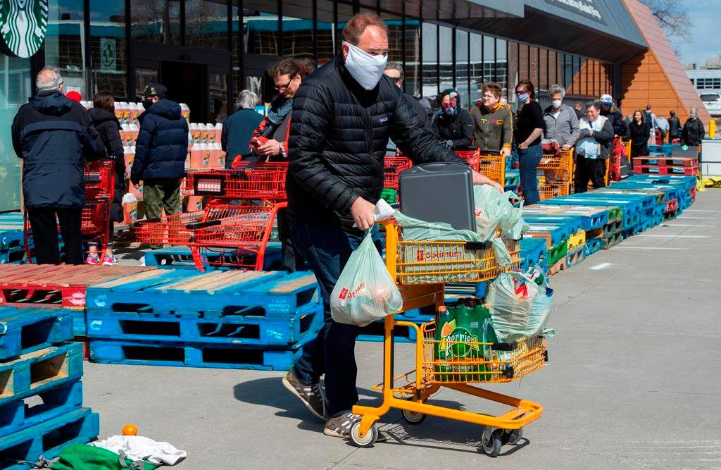 Long lines of masked shoppers wait to shop for groceries in Toronto on Thursday, April 9, 2020.
