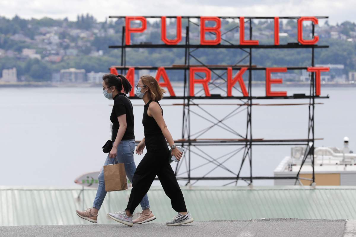 People wear masks as they cross a street Tuesday, July 7, 2020, near a sign for the Pike Place Market in Seattle. 