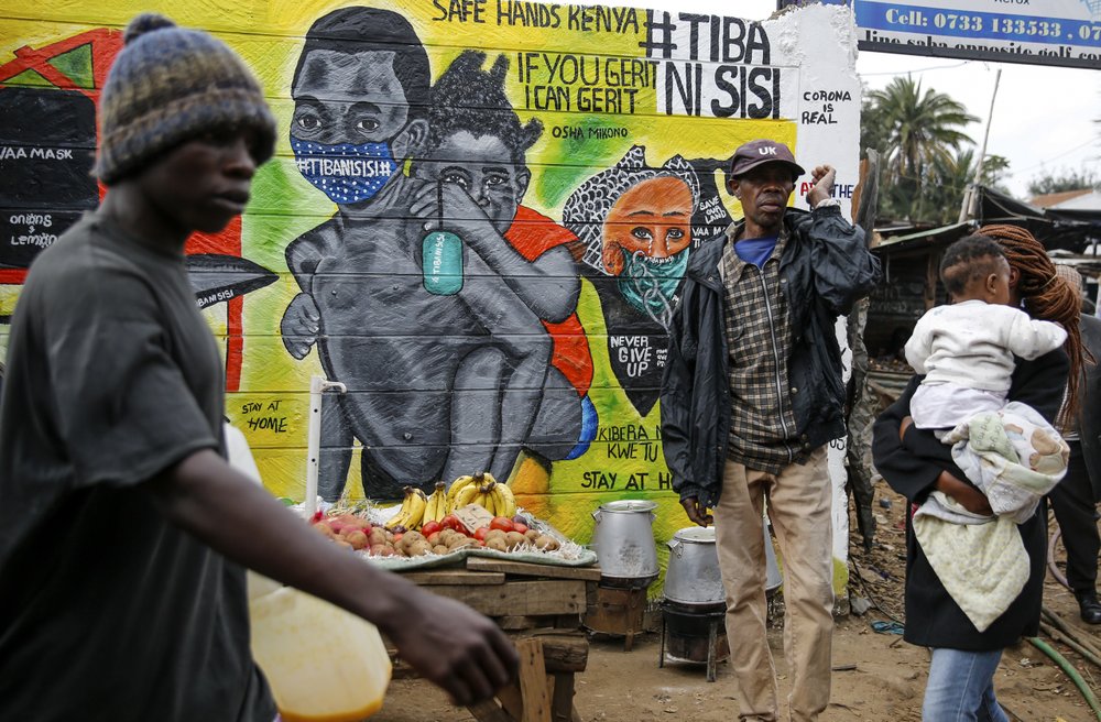 FILE - In this July 8, 2020, file photo, people walk past an informational mural warning people about the dangers of the new coronavirus and how to prevent transmission, with words in Swahili reading "We are the Cure", painted by youth artists from the Uweza Foundation, in the Kibera slum, or informal settlement, of Nairobi, Kenya. A dangerous stigma has sprung up around the coronavirus in Africa — fueled, in part, by severe quarantine rules in some countries as well as insufficient information about the virus. 