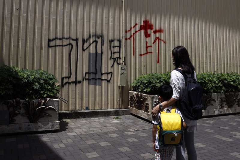 Pamela Lam and her son stand in Hong Kong, Friday, July 3, 2020. Lam's 6-year-old son fell in love with the Hong Kong protest anthem, "Glory to Hong Kong," the first time he heard it and sings it quite often. The Chinese painted on wall reads: "See you on street at July 1." Lam agreed to be photographed only if her face was not shown, fearing possible retribution from authorities. 