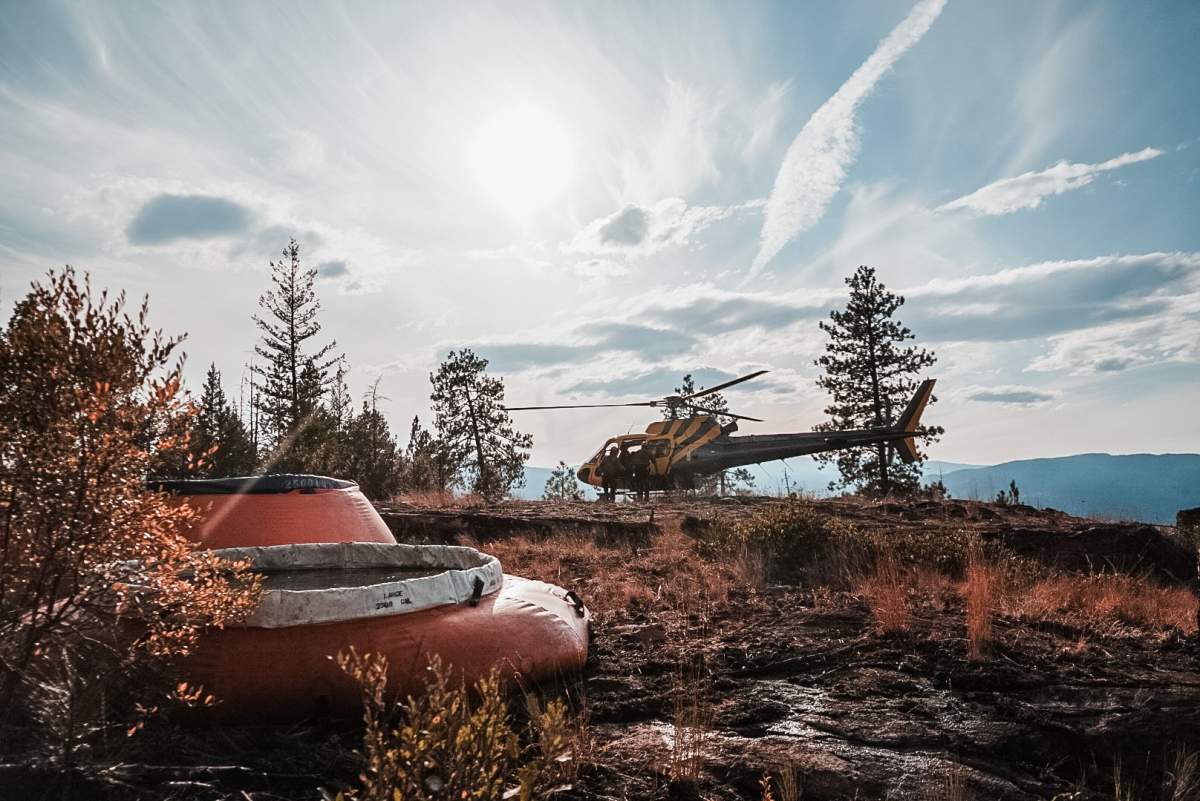 FILE. A helicopter landing beside some water bladders at a Penticton Wildfire. 