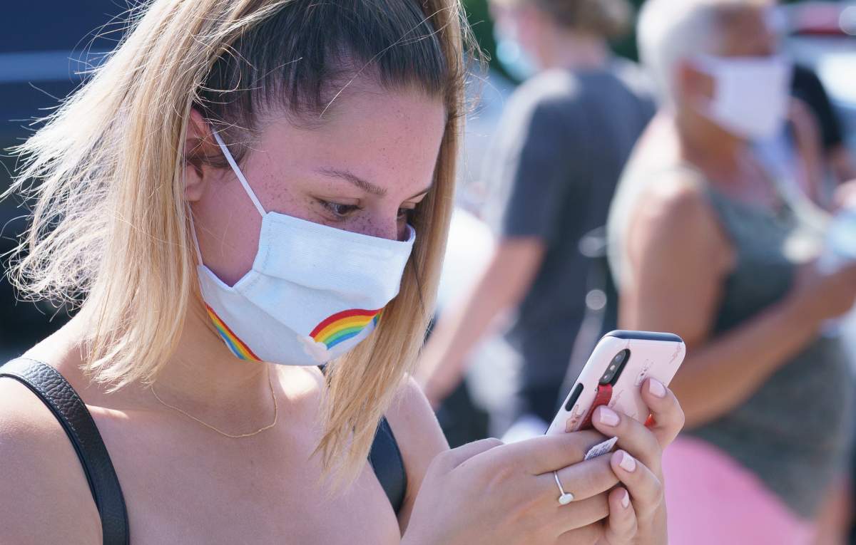 A woman checks her phone as she waits in line to enter a mobile COVID-19 test clinic in Mercier, Que., Thursday, July 9, 2020. 