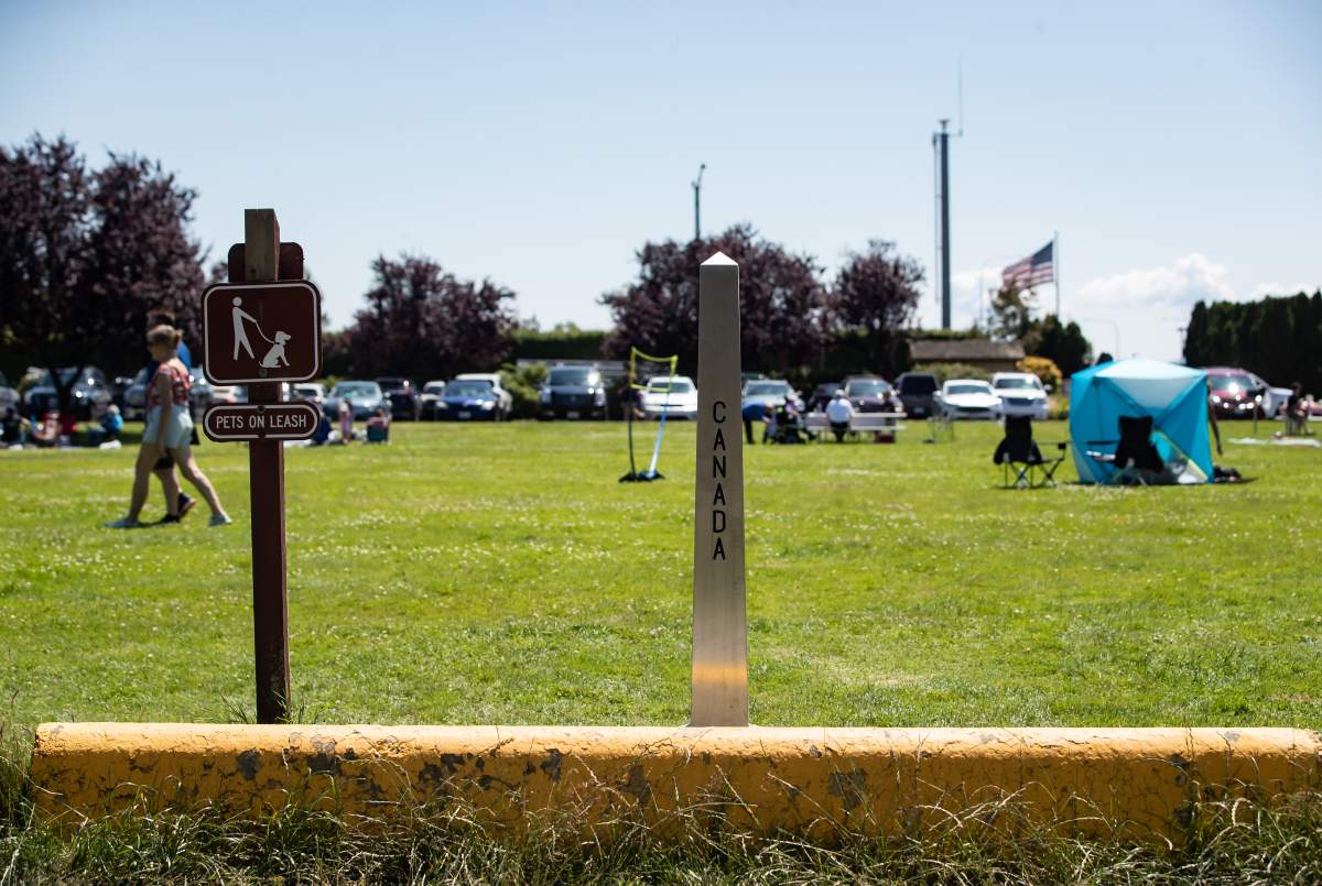 The COVID-19 pandemic has meant the Canada - U.S. border has been closed to regular cross-border shopping trips and vacations since May, and many American businesses near the border say they miss both the revenues and the Canadians. A Canada-U.S. border marker is seen in Surrey, B.C., as people gather at Peace Arch Historical State Park in Blaine, Wash., Sunday, July 5, 2020.