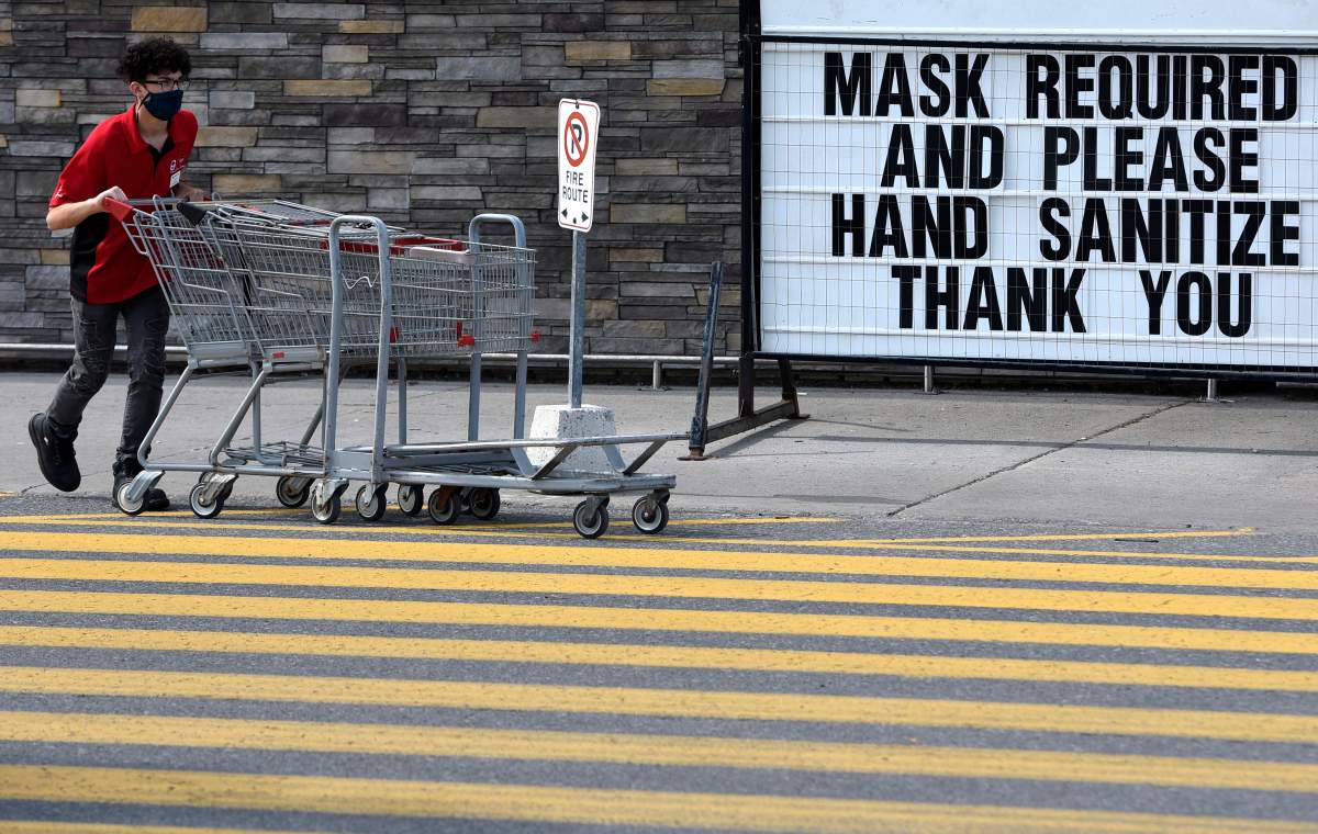 A staff member wears a mask as he collects carts at a store in Ottawa, on Saturday, Aug. 1, 2020, in the midst of the COVID-19 pandemic. 