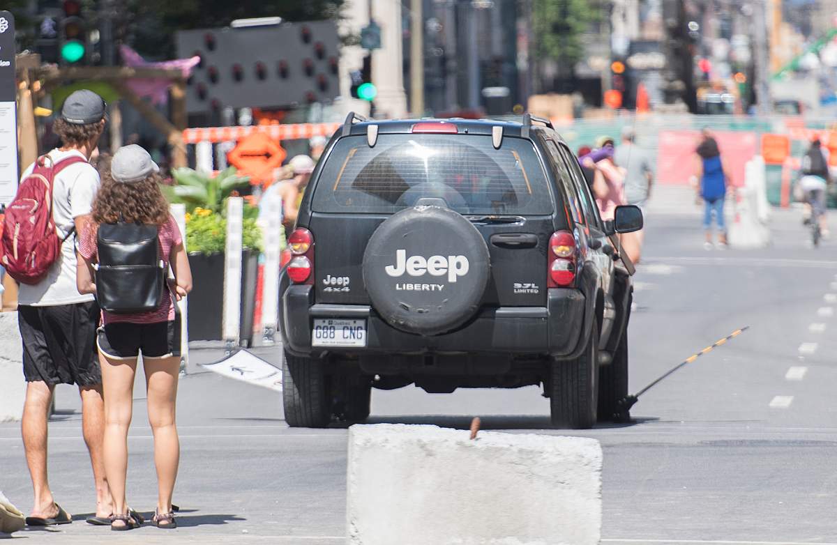 People look on as a jeep speeds down a pedestrian zone on Sainte-Catherine Street in Montreal, Saturday, Aug. 8, 2020.