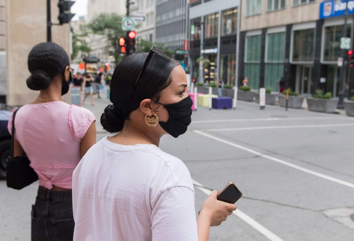 People wear face masks as they wait to cross a street in Montreal, Sunday, August 9, 2020, as the COVID-19 pandemic continues in Canada and around the world. 