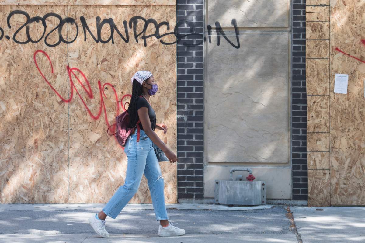 A woman wears a face mask as she walks by a boarded-up storefront on a street in Montreal, Saturday, Aug. 1, 2020, as the COVID-19 pandemic continues in Canada and around the world. 