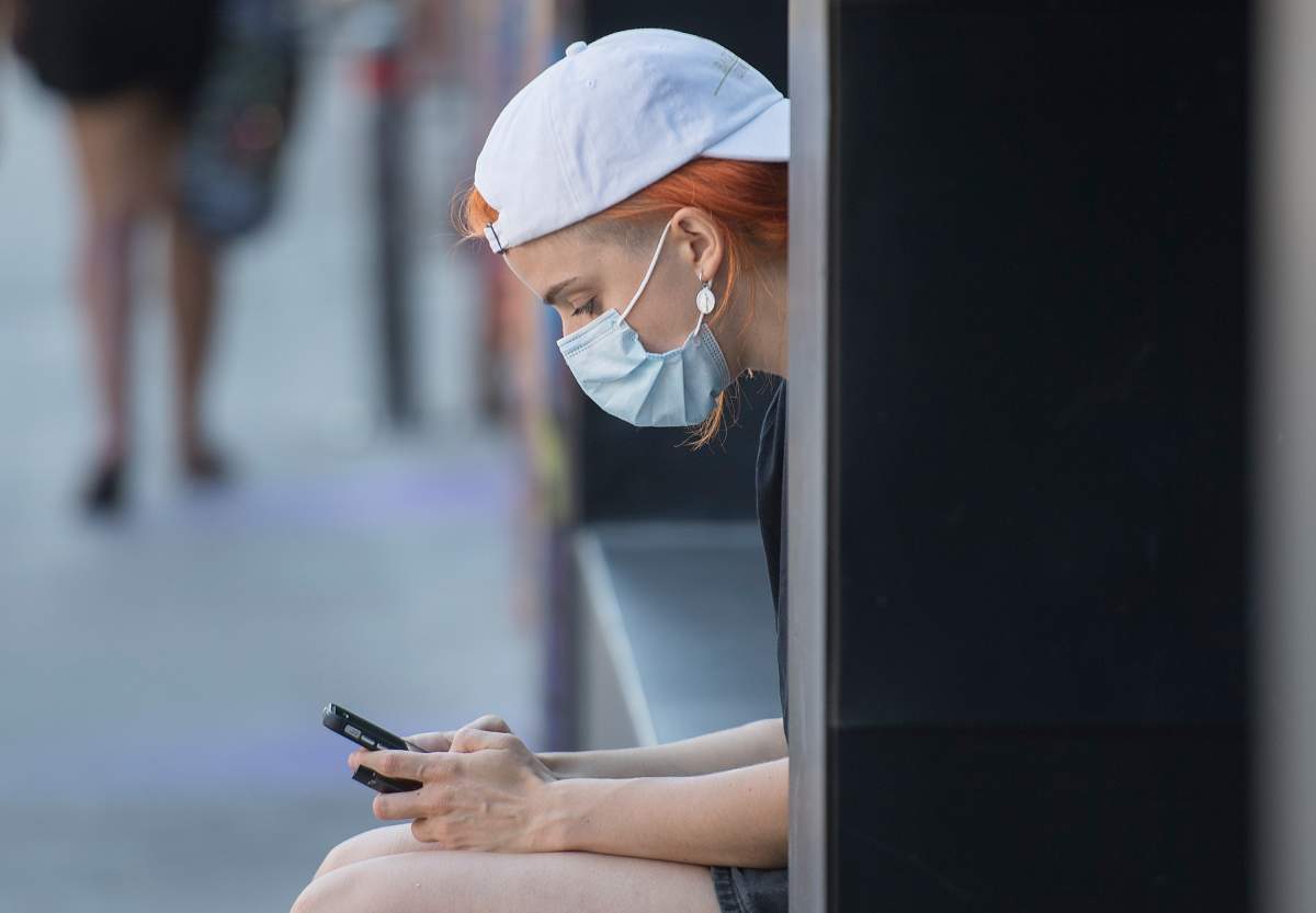 A woman wears a face mask as she browses on her phone in Montreal, Sunday, August 16, 2020, as the COVID-19 pandemic continues in Canada and around the world. 