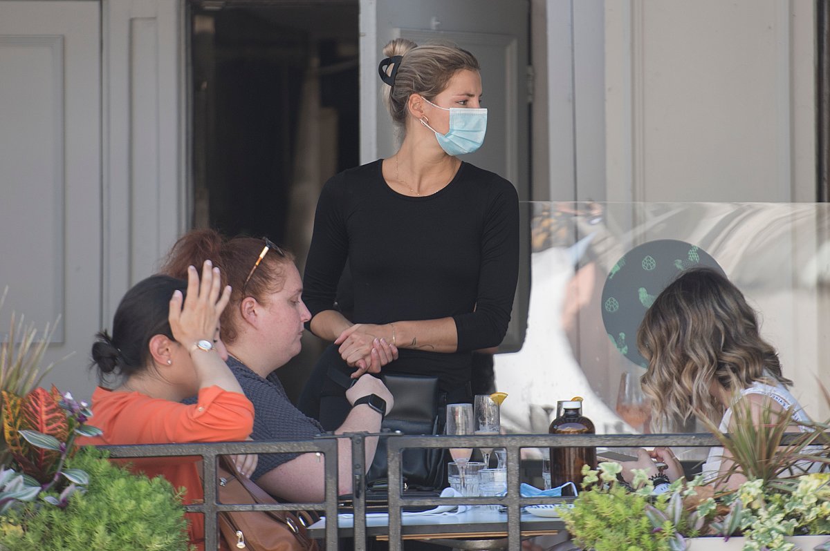 A server wears a face mask as customers pay for their meal at a restaurant in the Old Port of Montreal, Sunday, August 16, 2020, as the COVID-19 pandemic continues in Canada and around the world. 