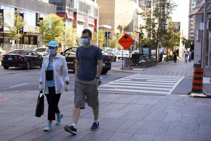 A man and woman wearing protective face masks walk along Bloor Street in Toronto on Aug. 29, 2020, amid the ongoing COVID-19 pandemic. 