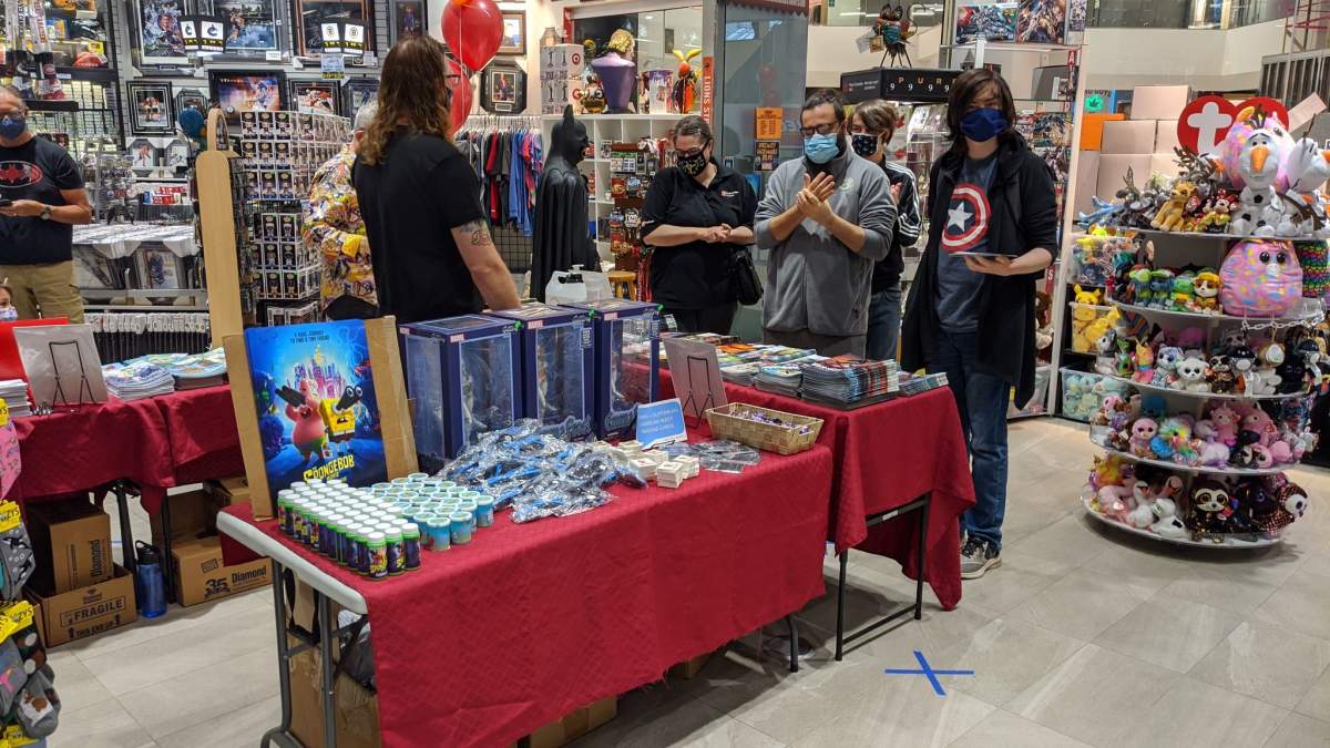 Customers wear masks and use hand sanitizer before selecting a free comic.