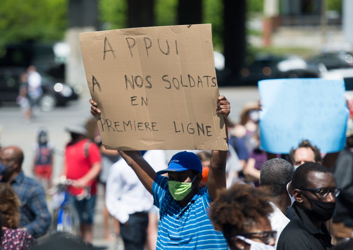 People hold up signs during a demonstration outside Prime Minister Justin Trudeau's constituency office in Montreal, Saturday, June 6, 2020, where they called on the government to give residency status to migrant workers as the COVID-19 pandemic continues in Canada and around the world. 