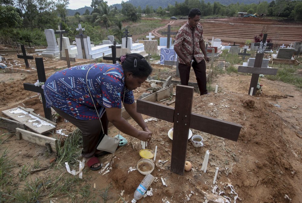 An Indonesian migrant worker places candles on the grave of her husband who worked on a Malaysian palm oil plantation in Sabah, Malaysia, on Sunday, Dec. 9, 2018.