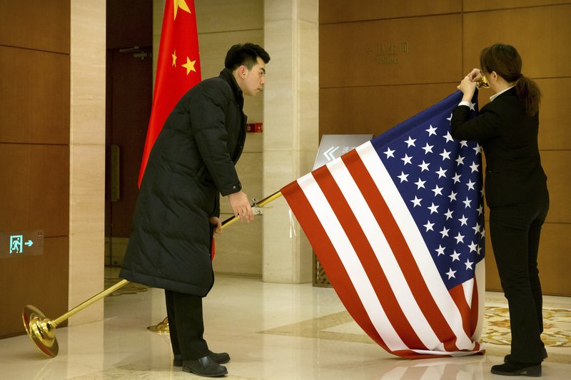 FILE - In this Feb. 14, 2019, file photo, Chinese staffers adjust a U.S. flag before the opening session of trade negotiations between U.S. and Chinese trade representatives at the Diaoyutai State Guesthouse in Beijing. China is delaying the renewal of press cards for at least five journalists working at four U.S. media outlets, an organization of foreign correspondents said Monday, Sept. 7, 2020 making them vulnerable to expulsion in apparent retribution for Washington's targeting of Chinese reporters working in the United States. 
