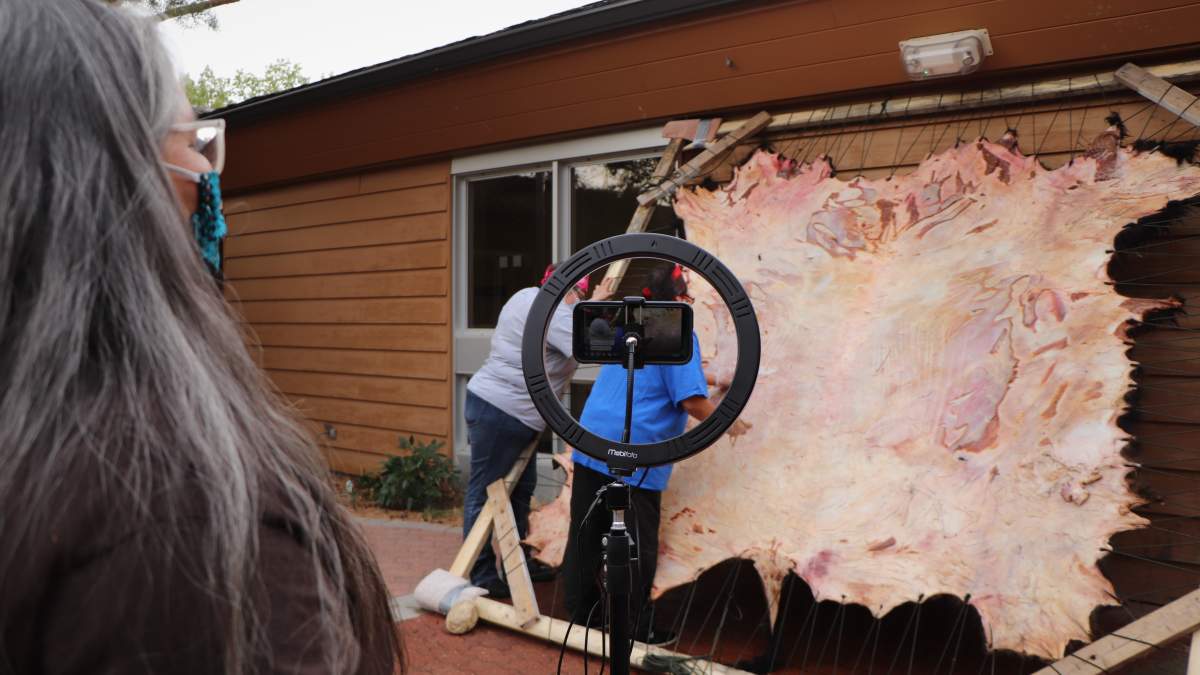 Joely BigEagle-Kequahtooway sets up a cellphone camera to livestream her buffalo hide workshop on Facebook
