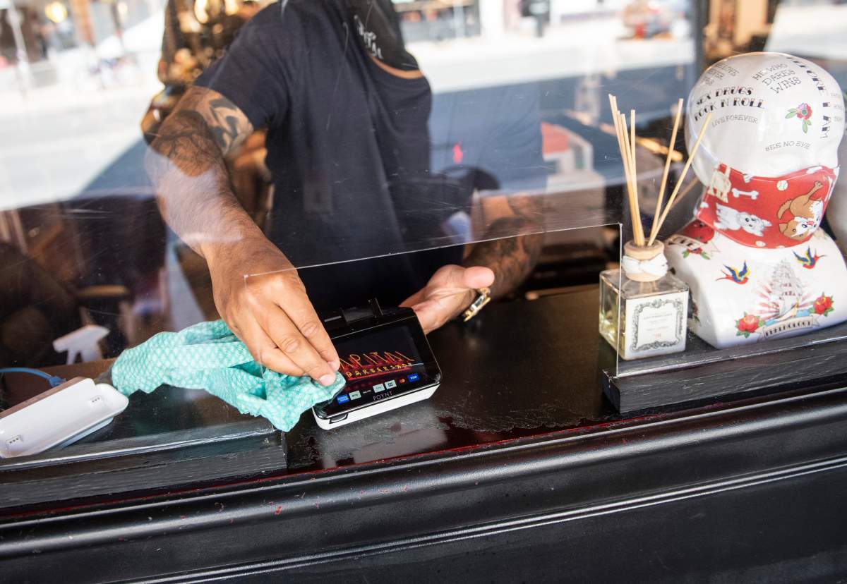 FILE - Owner Ankur Vadhera uses sanitizer on a credit card machine, at Capital Barber Shop in Ottawa, on its first day of reopening as Ontario moves into Stage 2 of its plan to lift lockdowns implemented in response to the COVID-19 pandemic, on Friday, June 12, 2020. 