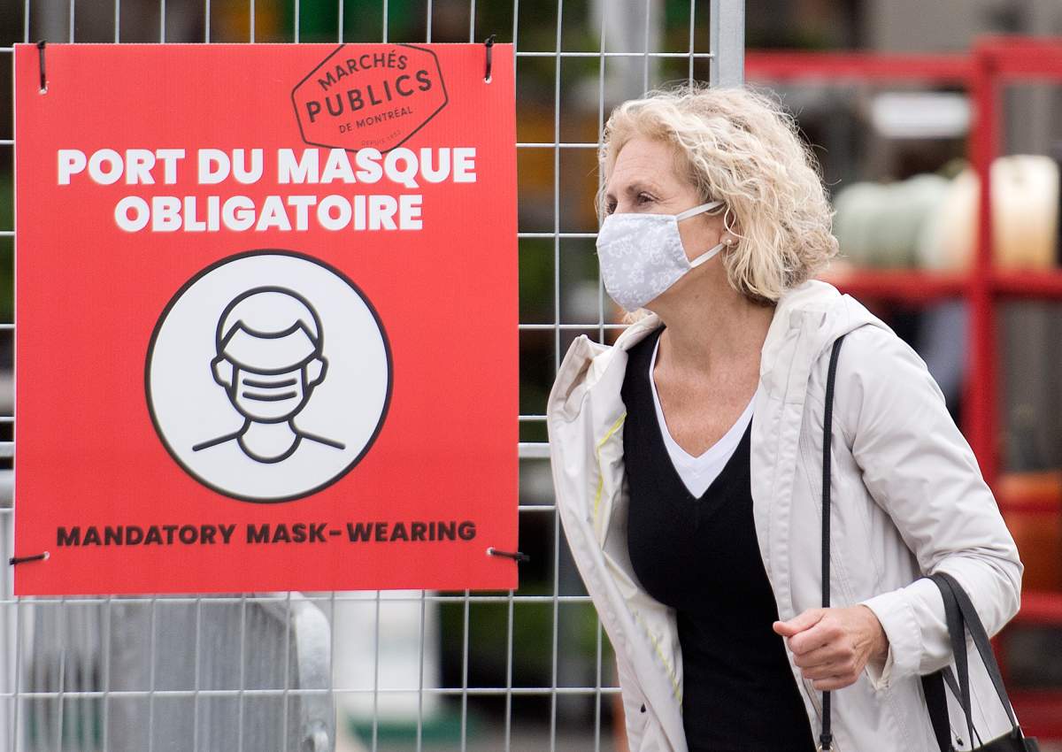 A woman wears a face mask as she walks by a sign instructing people to wear masks at a market in Montreal, Sunday, Sept. 13, 2020, as the COVID-19 pandemic continues in Canada and around the world.  