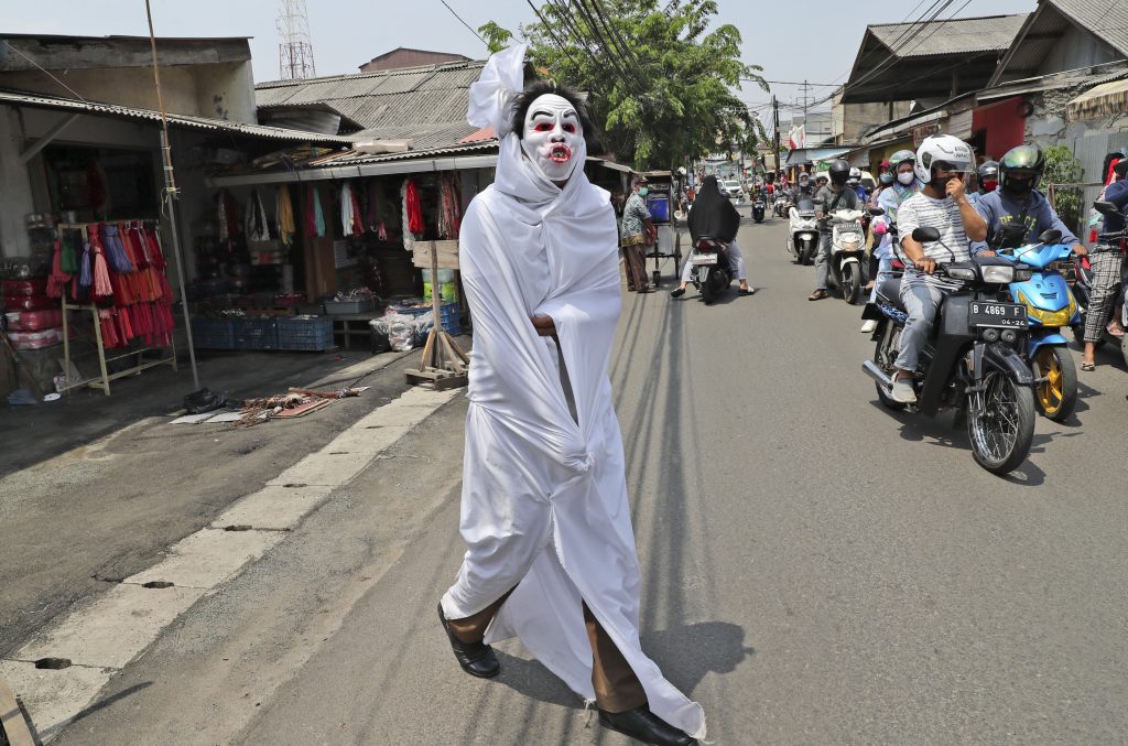 A government official dressed as a shrouded ghost, traditionally known as a 'pocong', to represent the victims of COVID-19 crosses a street during a coronavirus awareness campaign at a market in Tangerang, Indonesia, Wednesday, Sept. 16, 2020. 