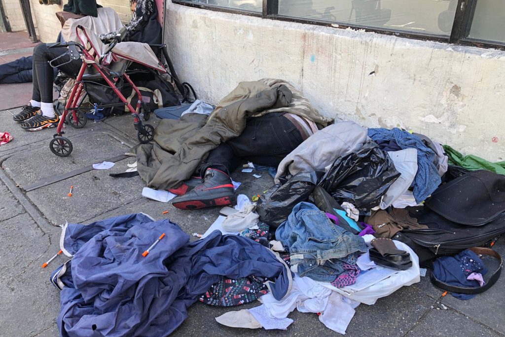 FILE - In this July 25, 2019, file photo, sleeping people, discarded clothes and used needles are seen on a street in the Tenderloin neighborhood in San Francisco. San Francisco has sued 28 alleged drug dealers who frequent a downtown neighborhood where broad daylight drug dealing and drug use is common to stop the flow of drugs. City Attorney Dennis Herrera said Thursday, Sept. 24, 2020, the suits are part of an effort to clean up the Tenderloin, which has seen the city's largest number of overdose deaths. 