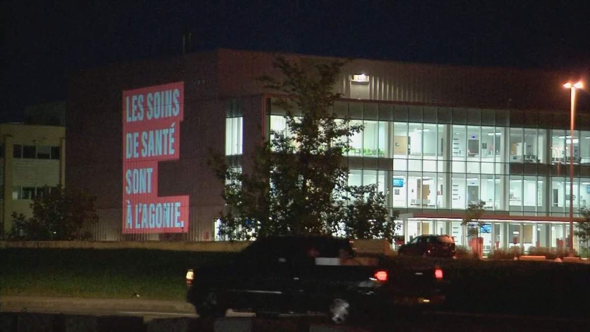 The Fédération interprofessionnelle de la santé du Québec (FIQ) broadcasts the slogan of its new advertising campaign, declaring the province's health care system to be 'in agony,' on the side of the Maisonneuve-Rosemont hospital in Montreal's east end on Sept. 15, 2020.