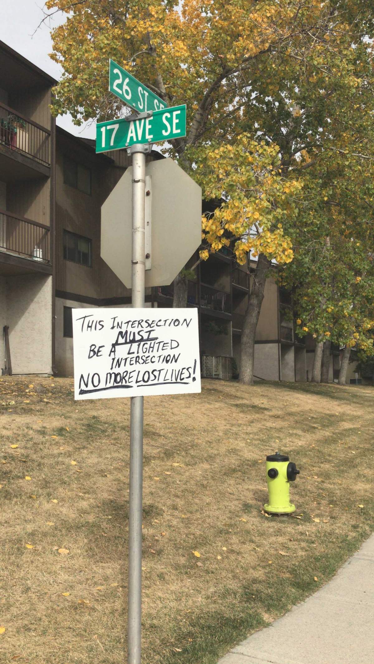 A hand-written sign posted on a stop sign calls for traffic lights at an intersection near the scene of a fatal motorcycle collision on Barlow Trail.