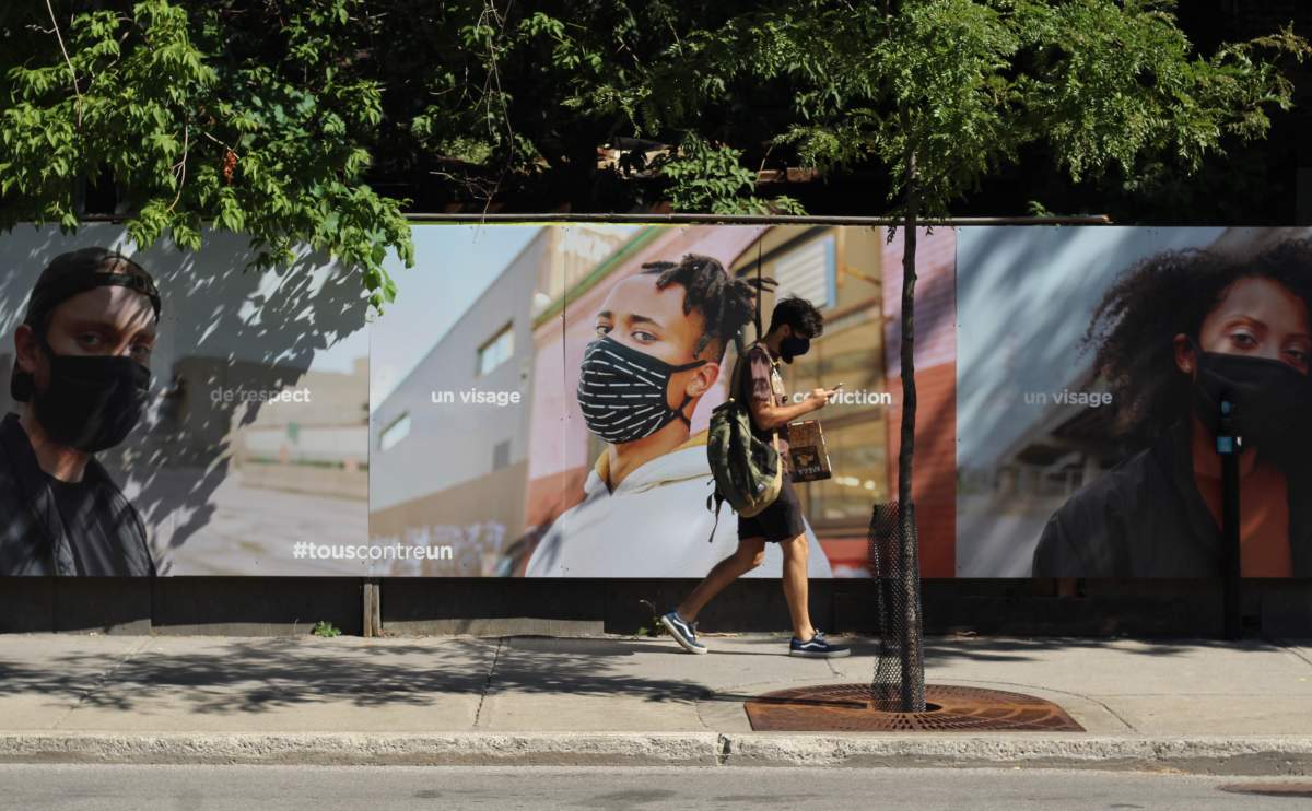 A pedestrian wearing a facemask walks past a series of billboards from the Quebec government urging residents to wear masks on Ontario Street East in Montreal's Gay Village.