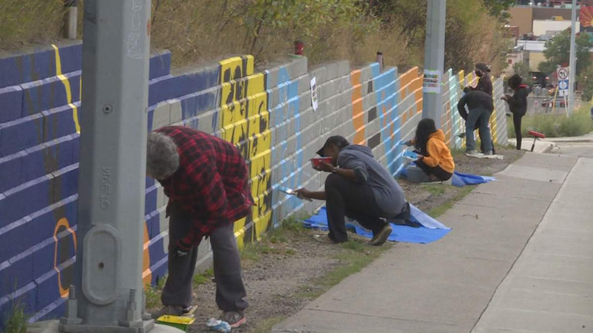 Painters work on the Centre Street retaining wall mural on Sunday, Sept. 13, 2020.