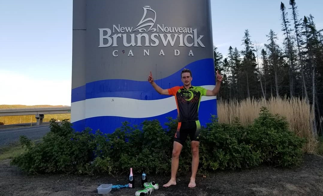 Jake Musgrave celebrates after completing his cross-Canada bike ride while wearing a mask. 