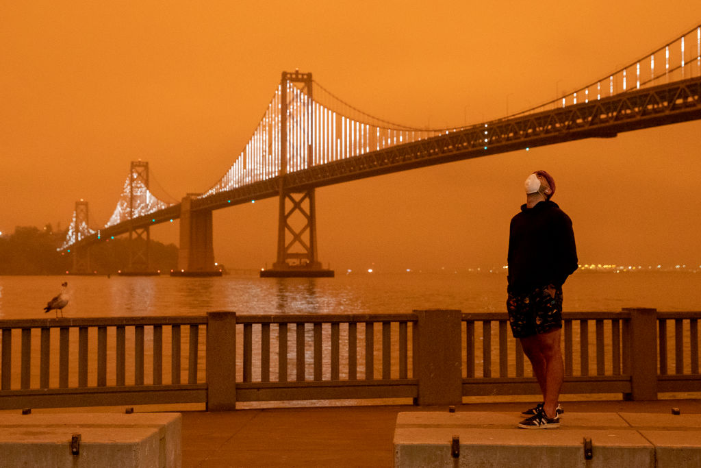 Eli Harik of San Francisco wears a mask while looking up at the dark orange sky hanging over the Embarcadero in downtown San Francisco, Calif., Wednesday, Sept. 9, 2020 due to multiple wildfires burning across California and Oregon.