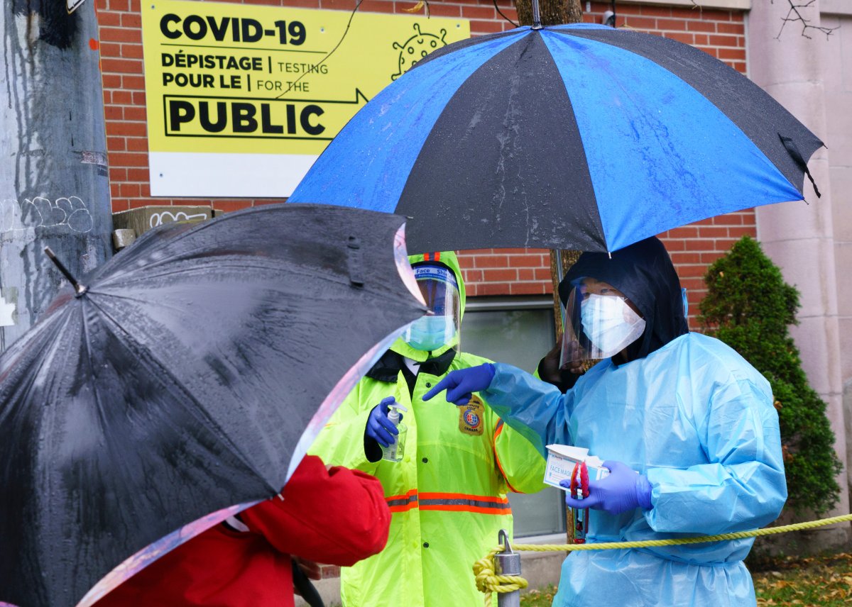 A health-care worker hands out masks to people waiting in line in the pouring rain outside a walk-in COVID-19 test clinic in Montreal, on Wednesday, October 7, 2020.