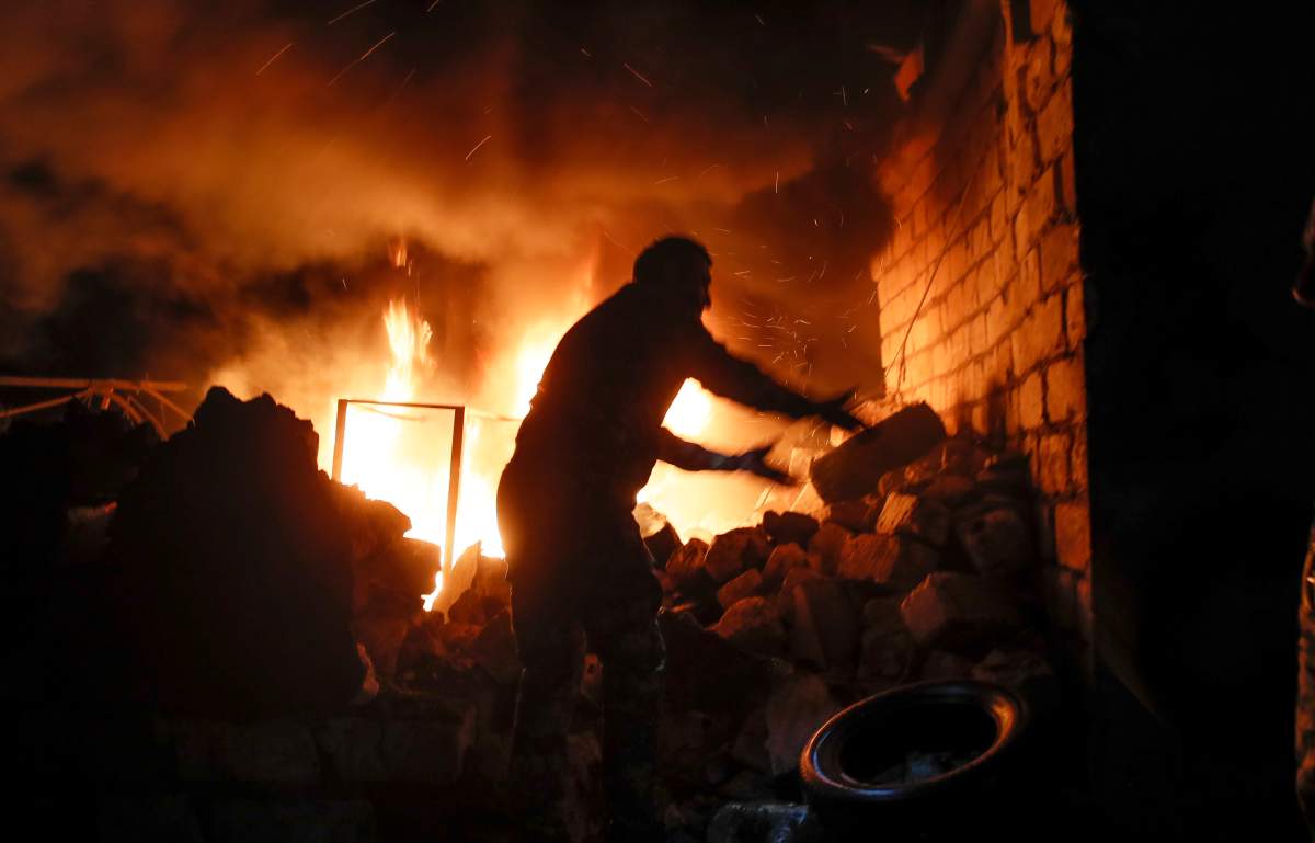 People try to remove car tyres from a car shop on fire after shelling by Azerbaijan’s artillery during a military conflict in Stepanakert, the separatist region of Nagorno-Karabakh, Oct. 23, 2020.