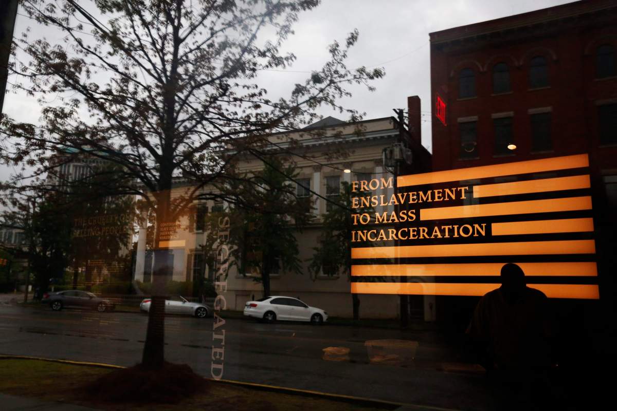 A man inside the Justice and the Legacy Museum is reflected on the front door, as an outside view is seen through the door in Montgomery, Ala., April 22, 2018.