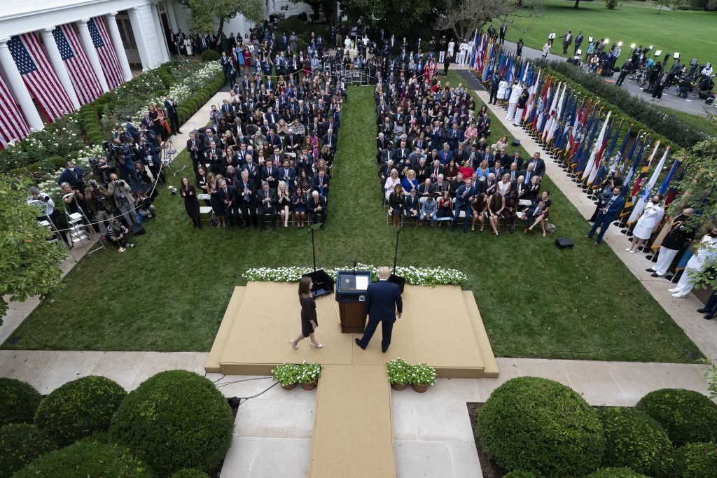 Judge Amy Coney Barrett walks to the microphone after President Donald Trump, right, announced Barrett as his nominee to the Supreme Court, in the Rose Garden at the White House, Saturday, Sept. 26, 2020, in Washington. Vice President Mike Pence is sitting in the front row on the left side of the center aisle.