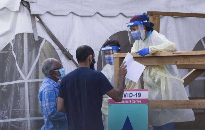 A medical worker wearing protective gear helps people register at a COVID-19 assessment center in Toronto on Sept. 25, 2020.