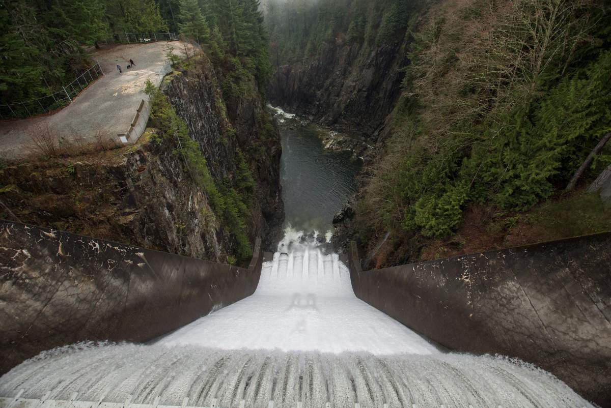 Water flows over the Cleveland Dam as people walk with a dog in Cleveland Park in North Vancouver, B.C., on Christmas Day, Friday Dec. 25, 2015. 