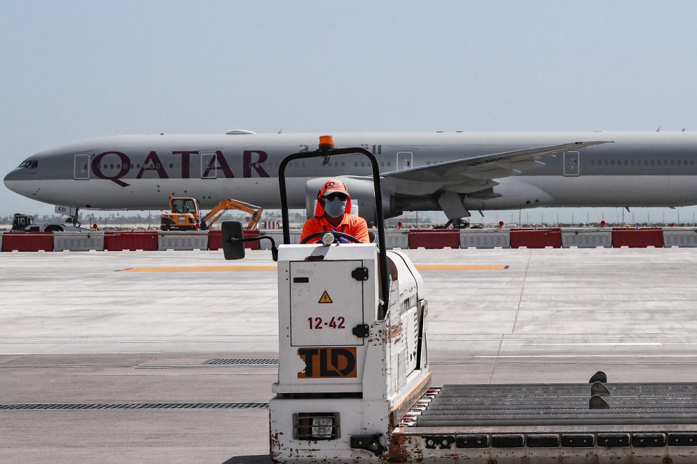 An airport worker mans a luggage trolley while behind him is seen a Qatar Airways Boeing 777 aircraft at Hamad International Airport in the Qatari capital Doha on April 1, 2020. 