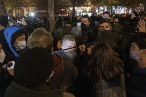 Migrants and activists face police officers, behind, Monday night Nov.23, 2020 on Place de la Republique in Paris.