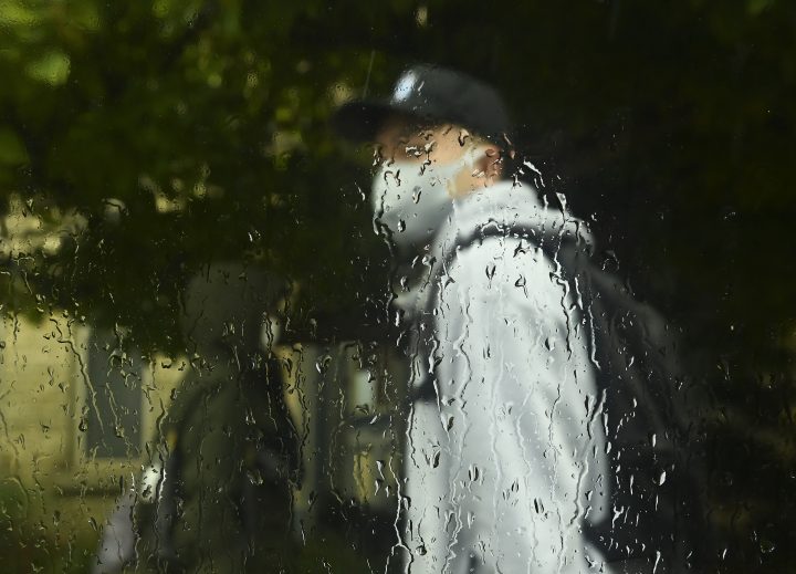 A person wearing a mask walks in the rain on a fall day during the COVID-19 pandemic in Toronto on Thursday, Oct. 15, 2020.