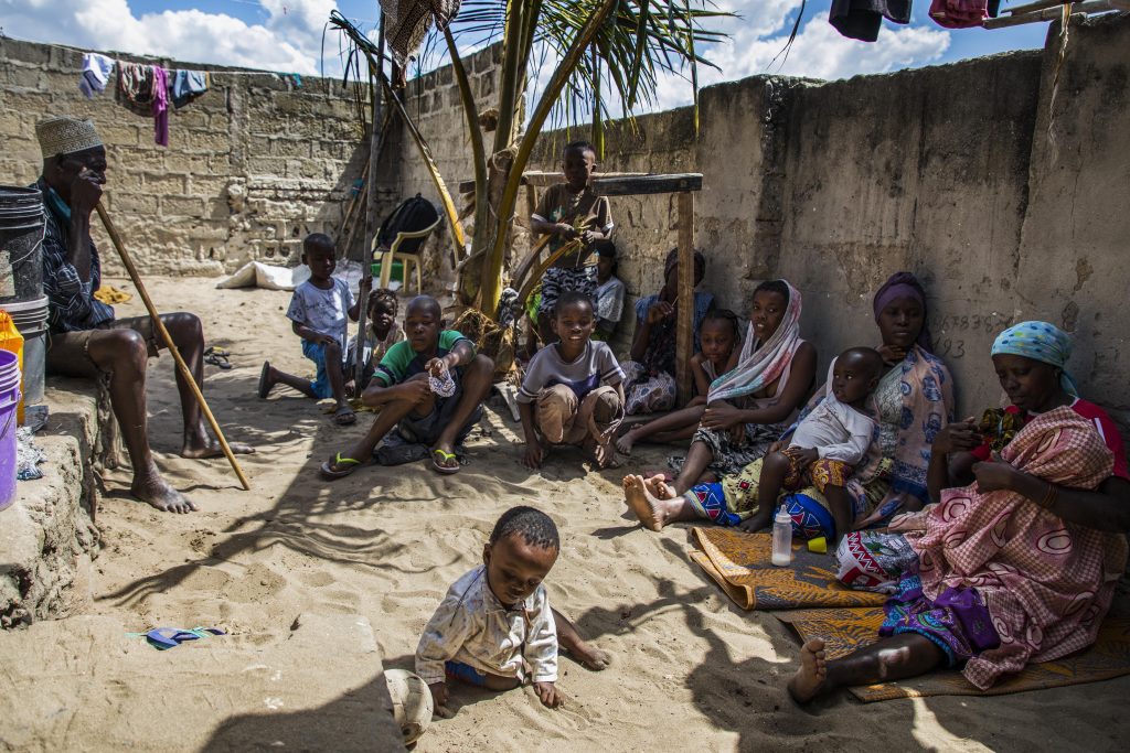 People sit outside an overcrowded house in an area that has become one of the main arrival points for displaced persons fleeing from armed violence raging in the province of Cabo Delgado, in the Paquitequete district of Pemba, northern Mozambique, 21 July 2020. Radical Islamist militant groups seeking to establish an Islamic state in the region, such as Ansar al-Sunna, have claimed responsibility for some of these attacks over the past year. The insurgent groups had taken control of strategic villages dotting the coast of the northern Cabo Delgado province – which are located more than 100 kilometers (62 miles) from the provincial capital, Pemba – for several days before they were driven out by troops belonging to the  Mozambique Defense Armed Forces (FADM).  