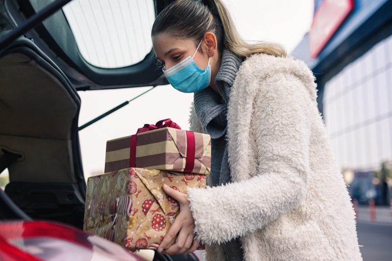 Teenage girl packing Christmas gifts in a car after shopping. She wears a protective mask to protect from COVID-19.