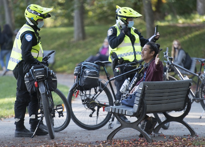 Police officers talk to a man at the Tam-Tams festival in Montreal, Sunday, October 4, 2020, as the COVID-19 pandemic continues in Canada and around the world.