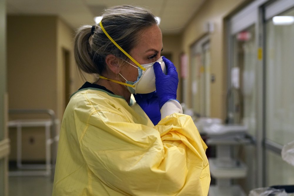 n this Nov. 24, 2020, file photo, registered nurse Chrissie Burkhiser puts on personal protective equipment as she prepares to treat a COVID-19 patient in the emergency room at Scotland County Hospital in Memphis, Mo. U.S. hospitals slammed with COVID-19 patients are trying to lure nurses and doctors out of retirement and recruiting nursing students and new graduates who have yet to earn their licenses. 